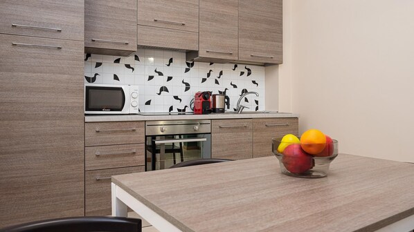 Cocina moderna con armarios de madera, microondas, hervidor y frutero en la encimera.