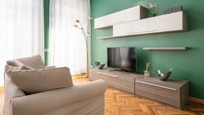 Een moderne woonkamer met een beige bank, een flatscreen televisie en een houten visgraatvloer.