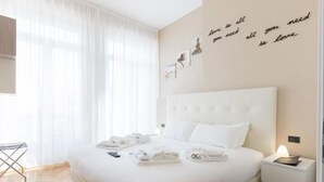 Une chambre d’hôtel avec un grand lit, du linge de lit blanc, une table de chevet avec une lampe et un mur orné de citations inspirantes.