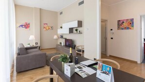 Un salon moderne avec un canapé gris, une table à manger avec des chaises et, au fond, un coin cuisine.