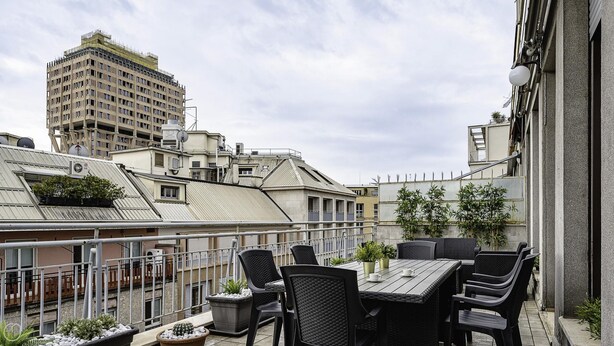 Une terrasse sur le toit, aménagée avec des espaces de détente en plein air, des plantes en pot et offrant une vue sur les bâtiments environnants.