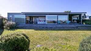 Ett modernt hus i två våningar med en stor entré bestående av en glasdörr, ett öppet köksområde och en uteplats med utemöbler.