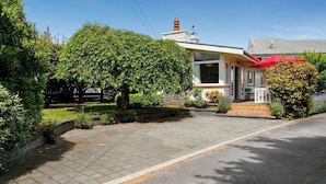 Une maison à deux étages avec un porche à l’avant, une cheminée et une allée menant à la porte d’entrée.