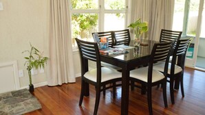 Un área de comedor con una mesa de vidrio rodeada por cuatro sillas, una planta en maceta y una ventana con cortinas.