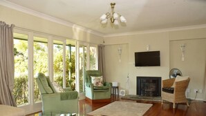 Una sala de estar con chimenea, sillones verdes, una mesa de centro de vidrio y un televisor montado en la pared.