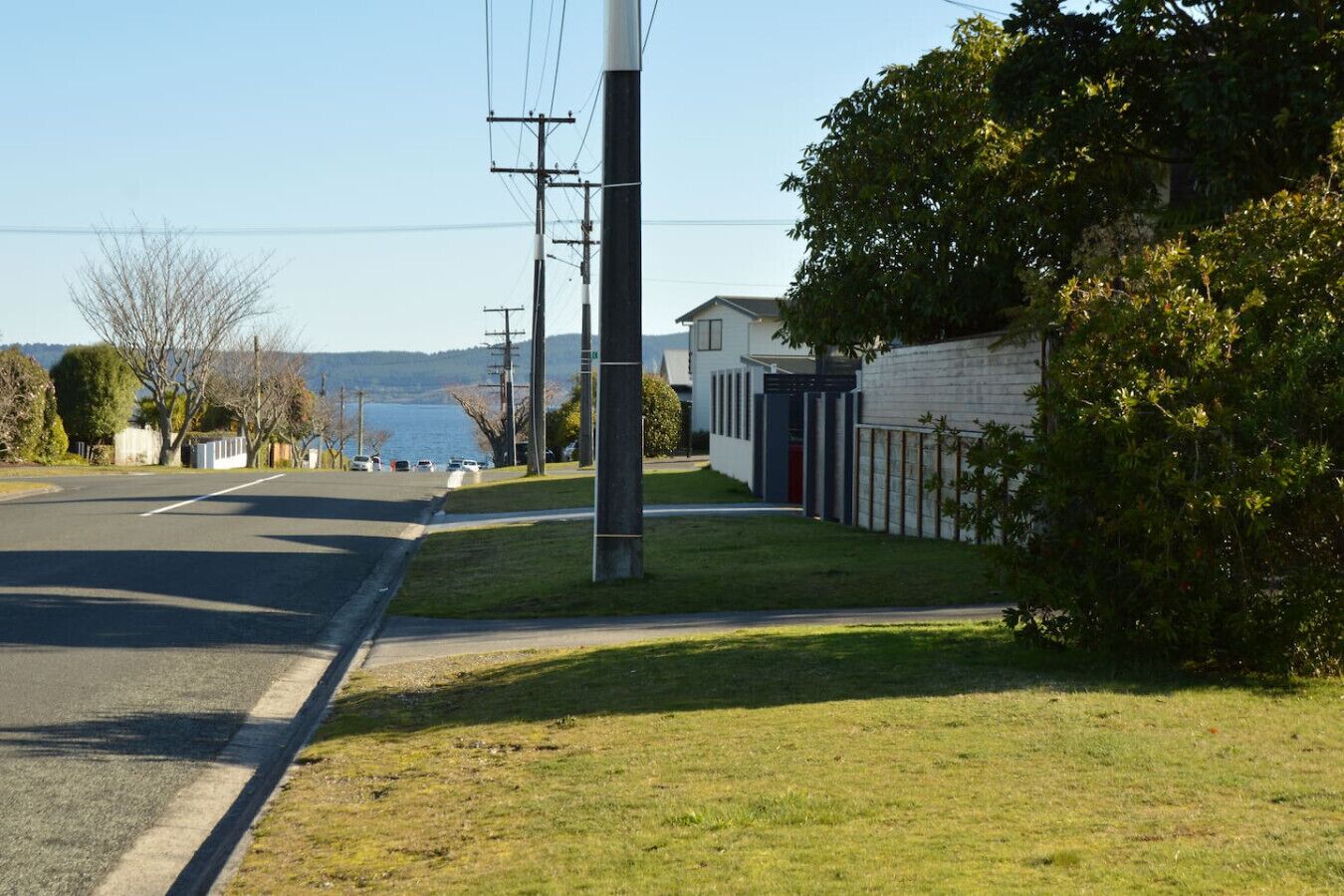 A residential street with houses, a grassy area, and a body of water in the background.