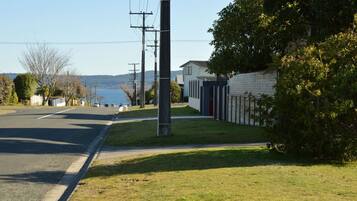 A residential street with houses, a grassy area, and a body of water in the background.