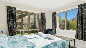 A hotel room with a large bed, a desk, and a chair. There are two windows with curtains, and a view of greenery outside. - Mercy of Lake Taupo- family time + lake time (Taupo)