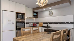 A modern kitchen with white cabinets, a stainless steel refrigerator, a microwave, an oven, a sink, and a wooden dining table with chairs. - Tui Unit - So close to the lake +Pool (Taupō)