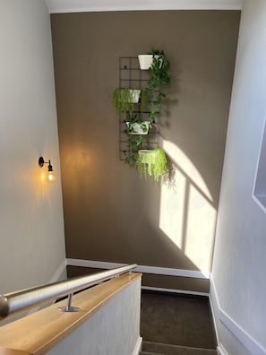 Staircase leads up to a cozy retreat with a wall-mounted shelf and lush greenery.