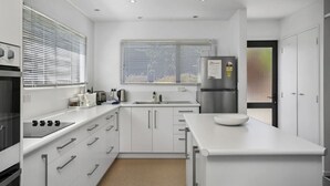 A modern kitchen with white cabinetry, a built-in oven, a stainless steel refrigerator, and a large window with blinds.
