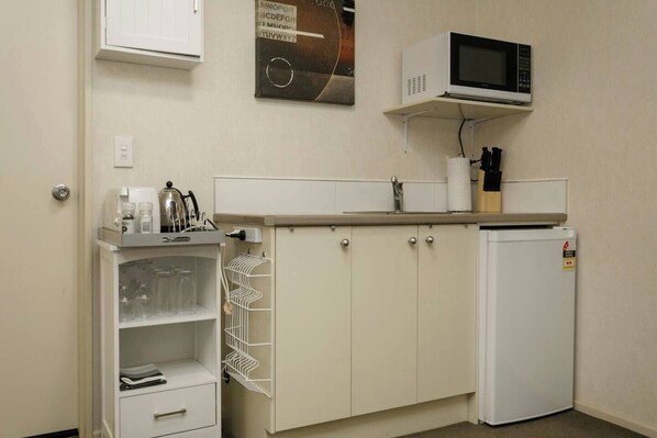 Una kitchenette compacta con microondas, un refrigerador pequeño, un lavamanos y un armario con espacio para vinos.