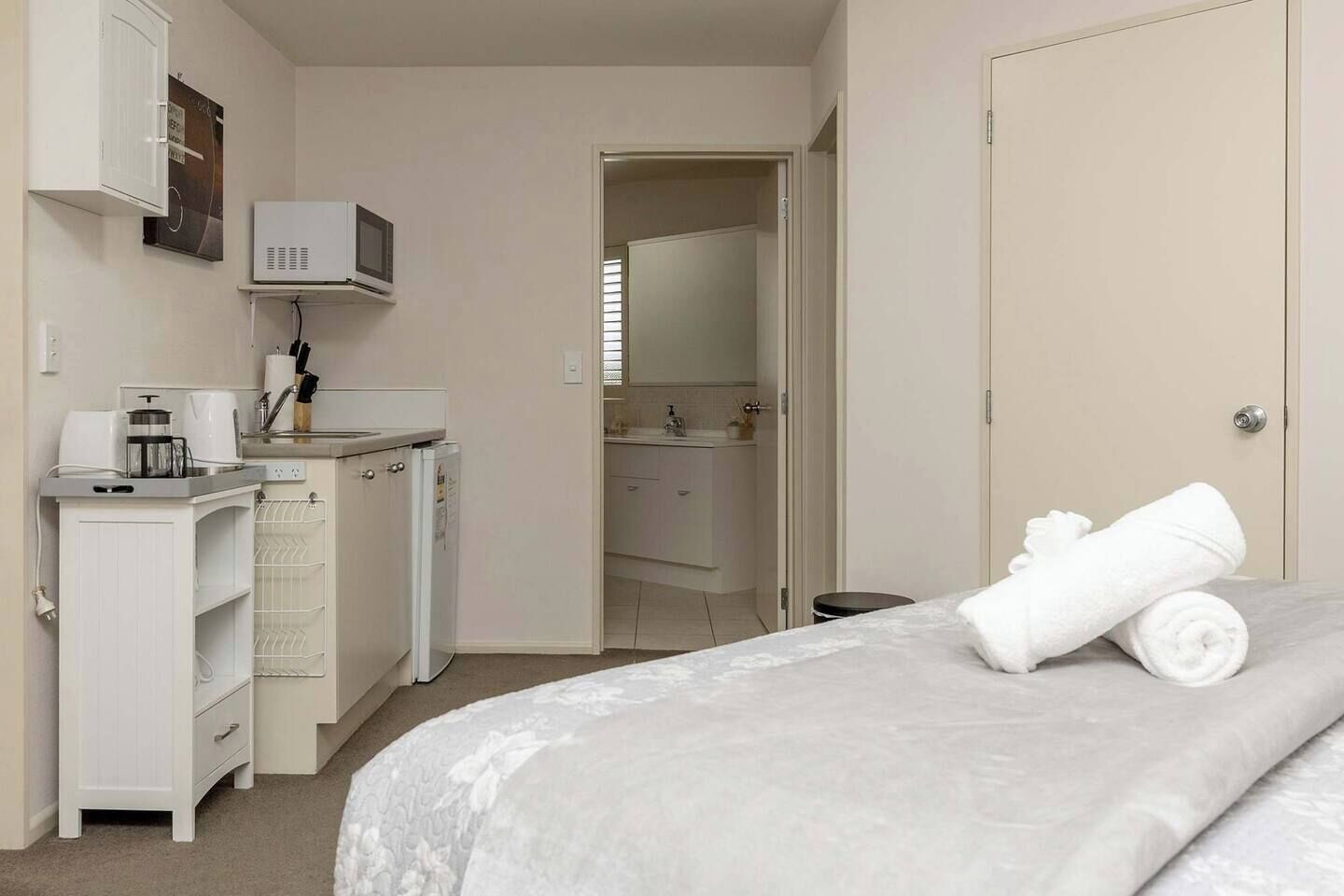 Une chambre à coucher avec un lit, un bureau doté d’une machine à café, un four à micro-ondes, et une salle de bain visible à travers une porte ouverte.