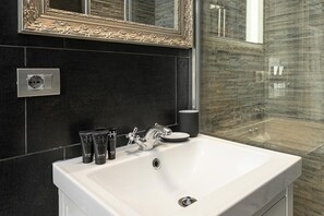 A bathroom with a white sink, black tiles, a gold-framed mirror, and toiletries on the counter.