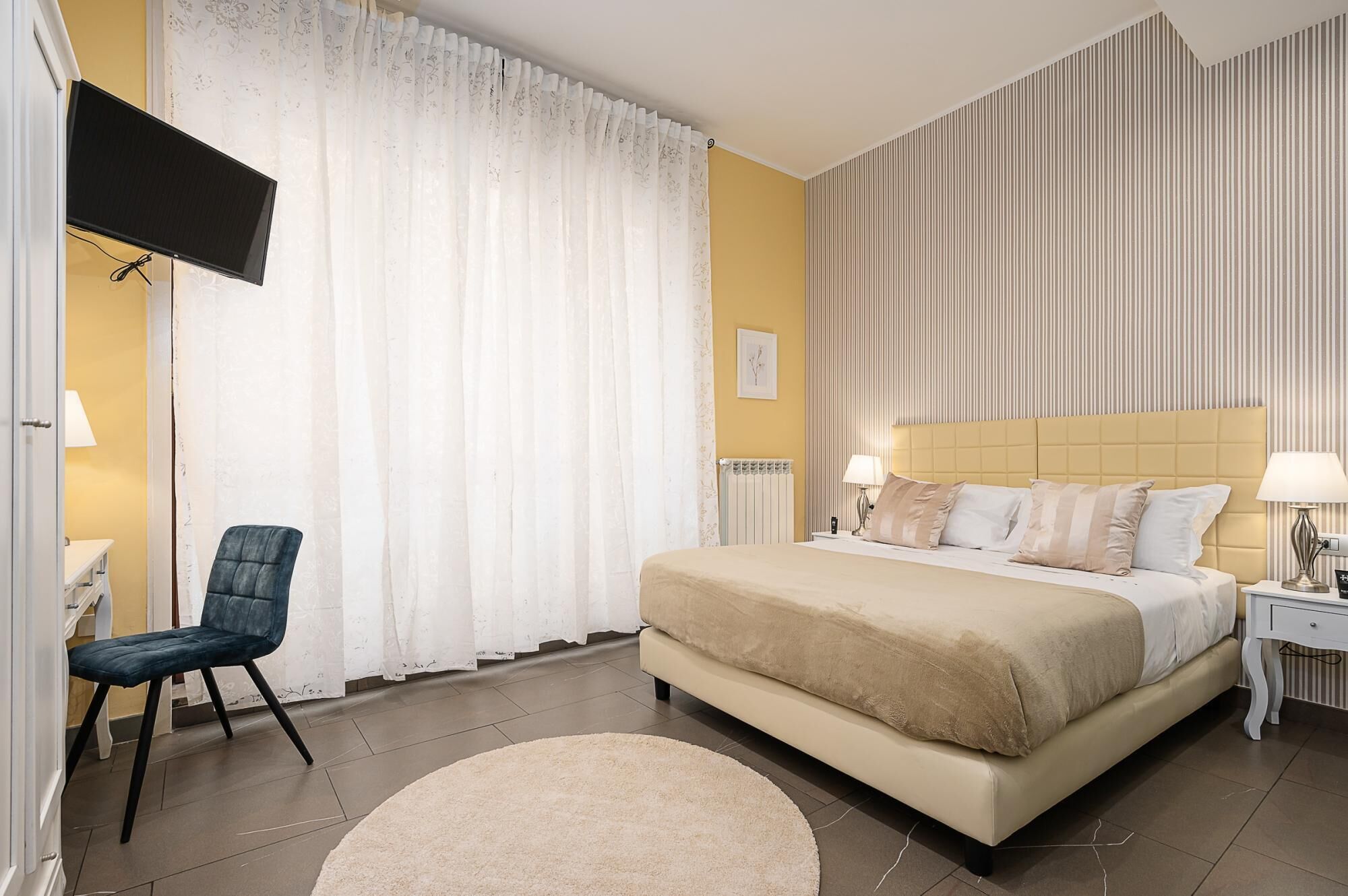A hotel room with a bed, a chair, a TV, a bedside table, and a lamp.