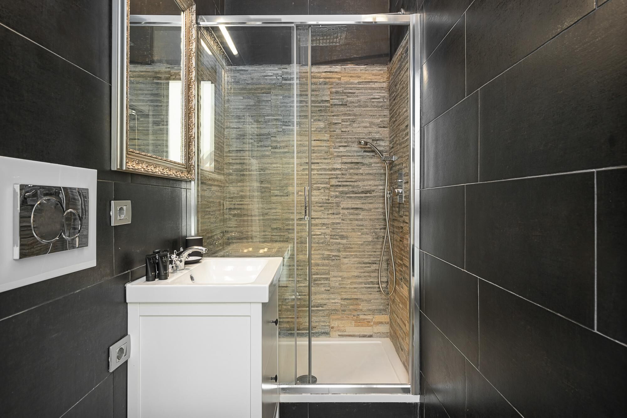 Un baño moderno con cabina de ducha de vidrio, un lavamanos blanco y un espejo con marco ornamentado.