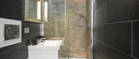 Un baño moderno con cabina de ducha de vidrio, un lavamanos blanco y un espejo con marco ornamentado.