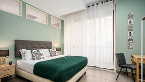 A bedroom with a bed, a chair, a desk, and a window with sheer curtains.