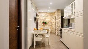 A narrow kitchen with white cabinets, a stone accent wall, and a dining area with a white table and chairs.