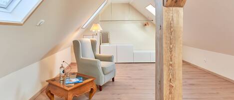 Amplio dormitorio tipo loft con techo inclinado, piso de madera, un ventanal grande, un escritorio, una silla y una lámpara.