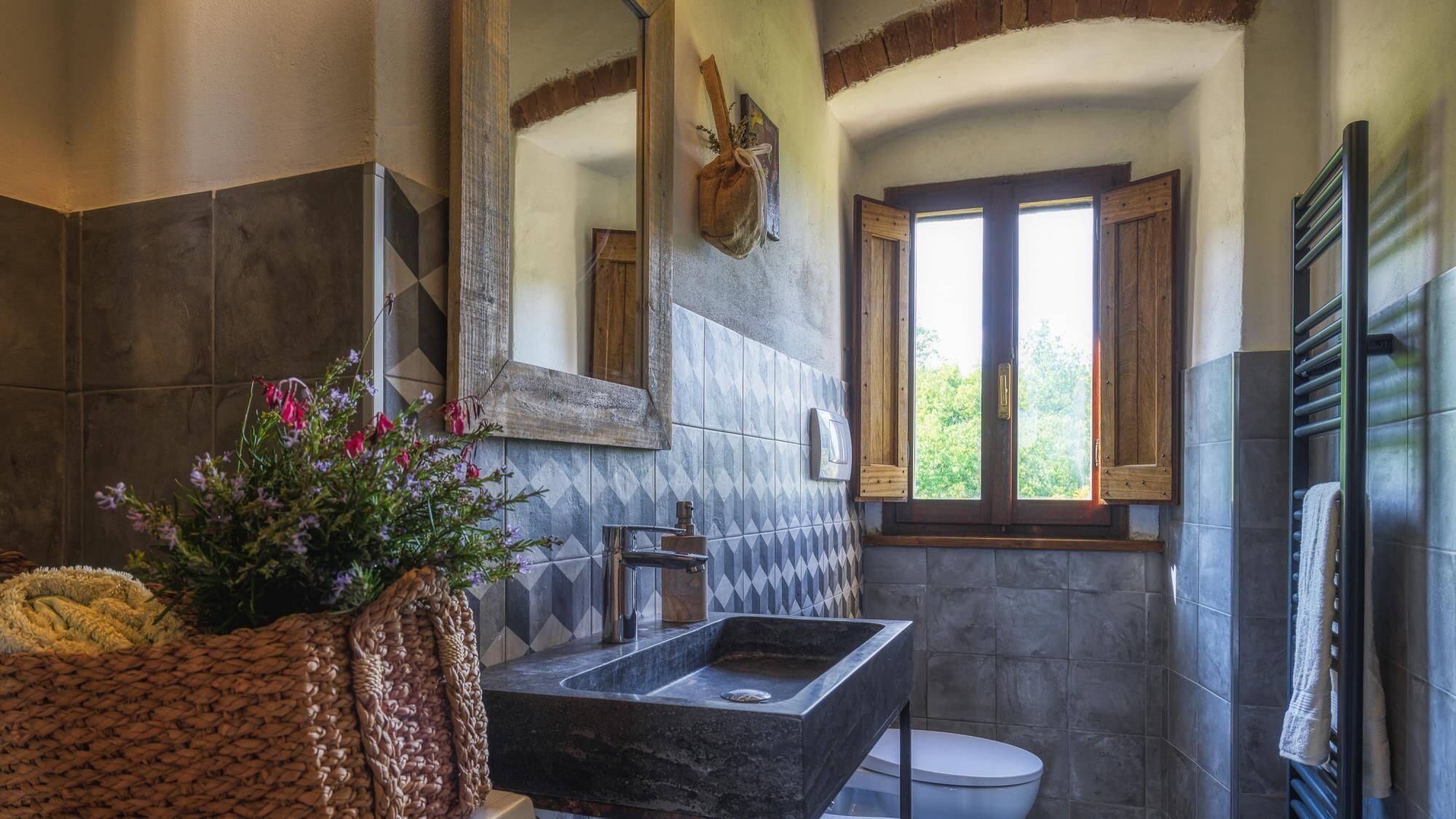 A bathroom with a large mirror, a sink, a toilet, and a window with wooden shutters.
