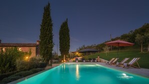 A swimming pool with lounge chairs and a covered area, surrounded by greenery and a building. - La Vecchia Pieve 8 in Pieve Caina (Marsciano)