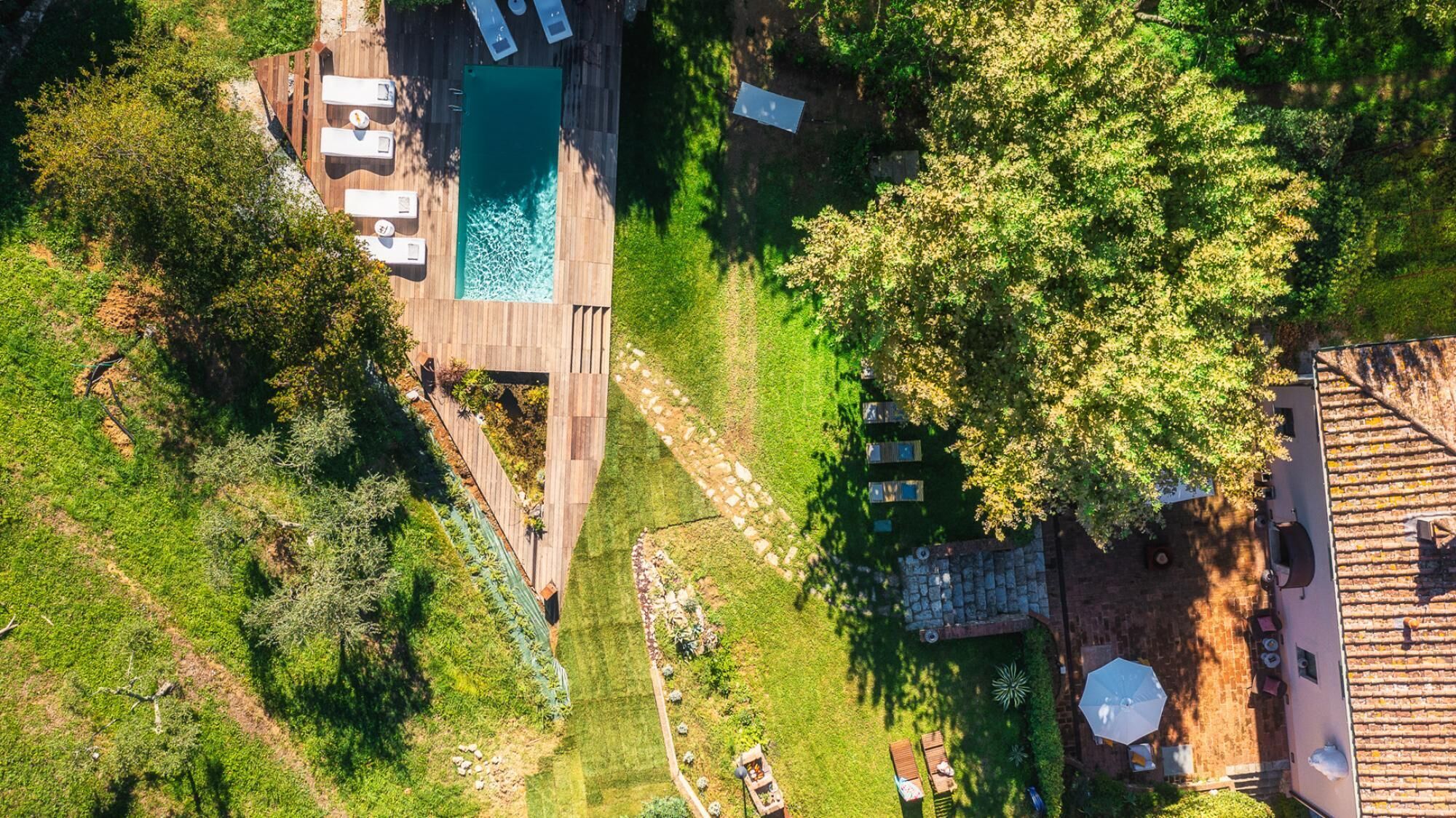 An aerial view of a property with a swimming pool, sun loungers, and a garden area.