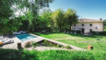 A pool with lounge chairs, a grassy lawn, and a building with a tiled roof.