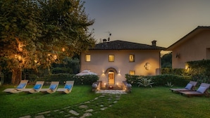 A house with a stone pathway leading to a front door, surrounded by a well-maintained lawn and outdoor seating area. - La Dama Del Bosco 8 3 (Pietrasanta)