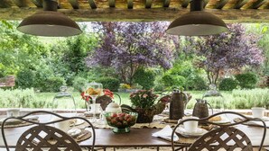 An outdoor dining area with a table set for two, surrounded by chairs, under a wooden pergola with hanging lamps. - Molino L Oppino 6 in Torrita di Siena (Torrita di Siena)