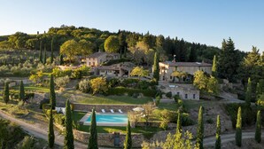 A hillside villa with a swimming pool, stone buildings, and a lush garden.