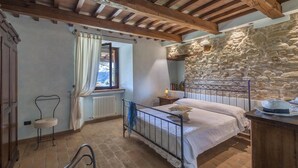 A bedroom with a stone wall, a bed with a metal headboard, a radiator, and a window with curtains. - Villa Il Baiocco 8 in Ospedaletto (Urbino)