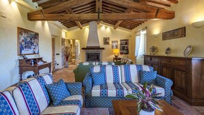 A cozy living room with a fireplace, a large sectional sofa, and a wooden ceiling. - Villa Il Baiocco 8 in Ospedaletto (Urbino)