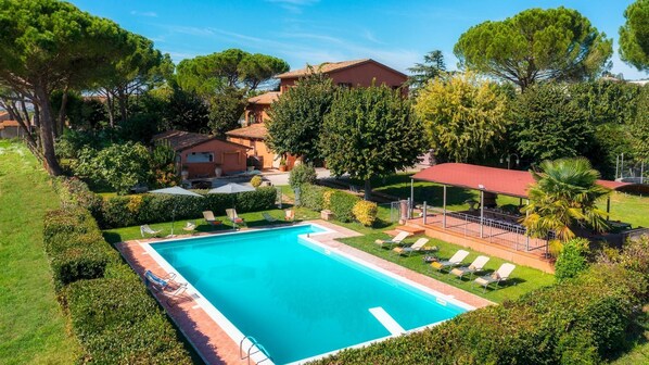 A rectangular swimming pool with a tiled deck, surrounded by well-maintained hedges and trees.