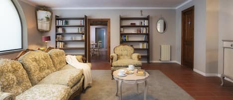 Una sala de estar con un sofá, sillones, una mesa de centro y estanterías llenas de libros.