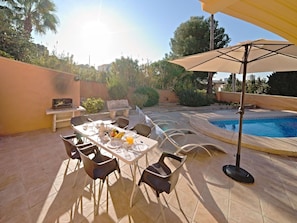 Eine Terrasse im Freien mit Esstisch, Stühlen, Pool und Bank.
