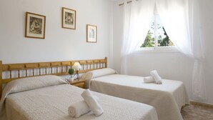 Een hotelkamer met twee bedden, een nachtkastje met een lamp en een raam met gordijnen.