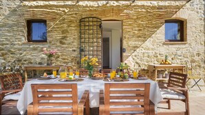 Un espacio para comer al aire libre con paredes de piedra, una mesa dispuesta para el desayuno y sillas de madera.