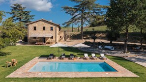 A stone house with a swimming pool, outdoor seating, and a grassy lawn.