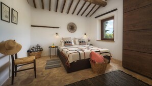 Un dormitorio acogedor con suelo de piedra, cama con ropa de cama estampada, un ventanal grande y un techo rústico.