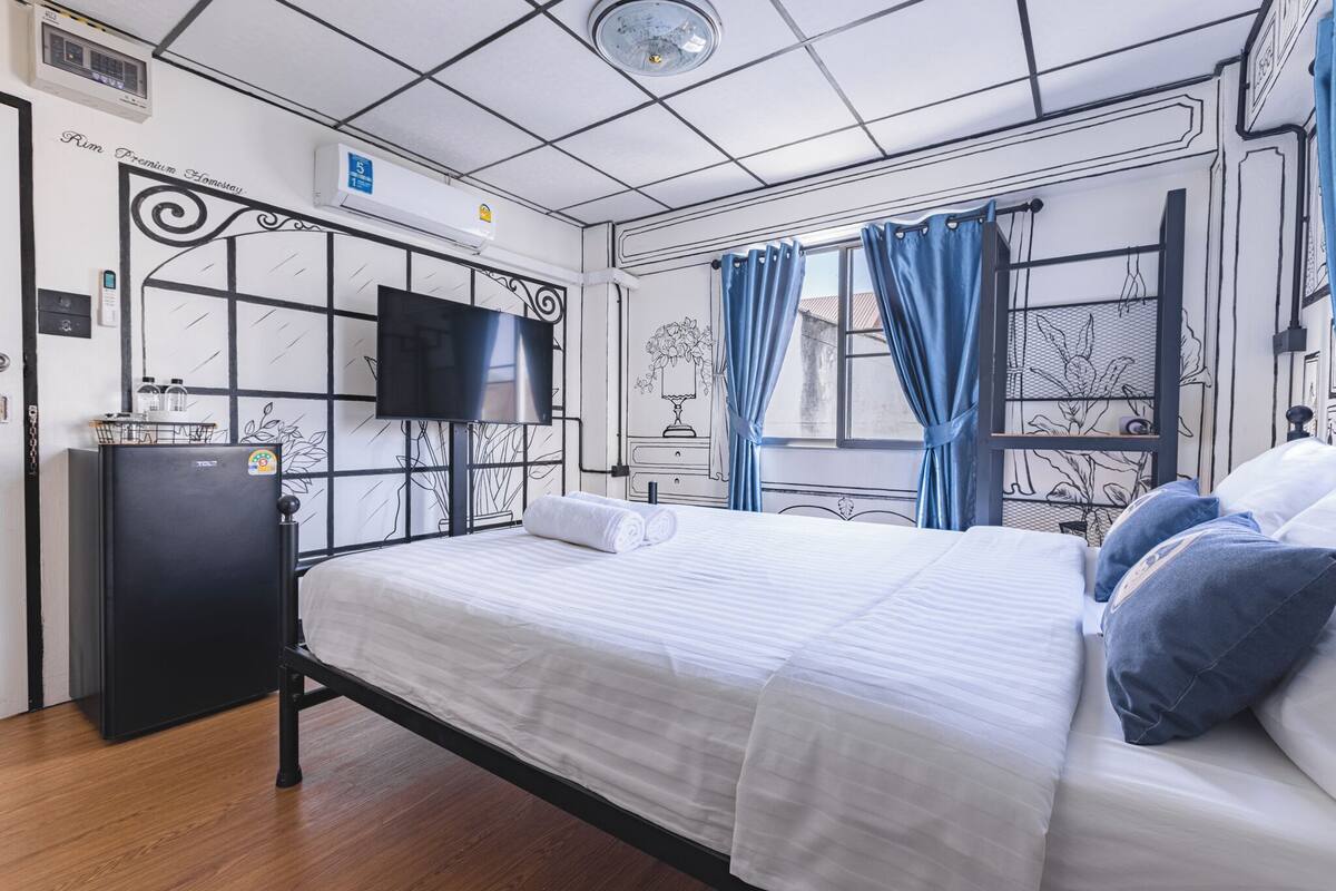 Une chambre d’hôtel avec un lit, une télévision, un petit réfrigérateur et une fenêtre avec des rideaux.