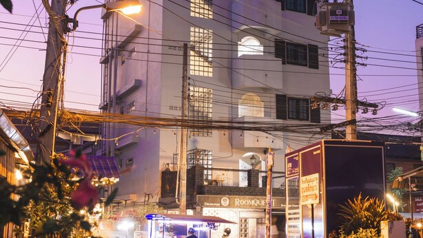 A multi-story building with a prominent entrance, a visible shop on the ground floor, and a parked scooter in front. - RoomQuest Chiang Mai Tha Phae (Chiang Mai)