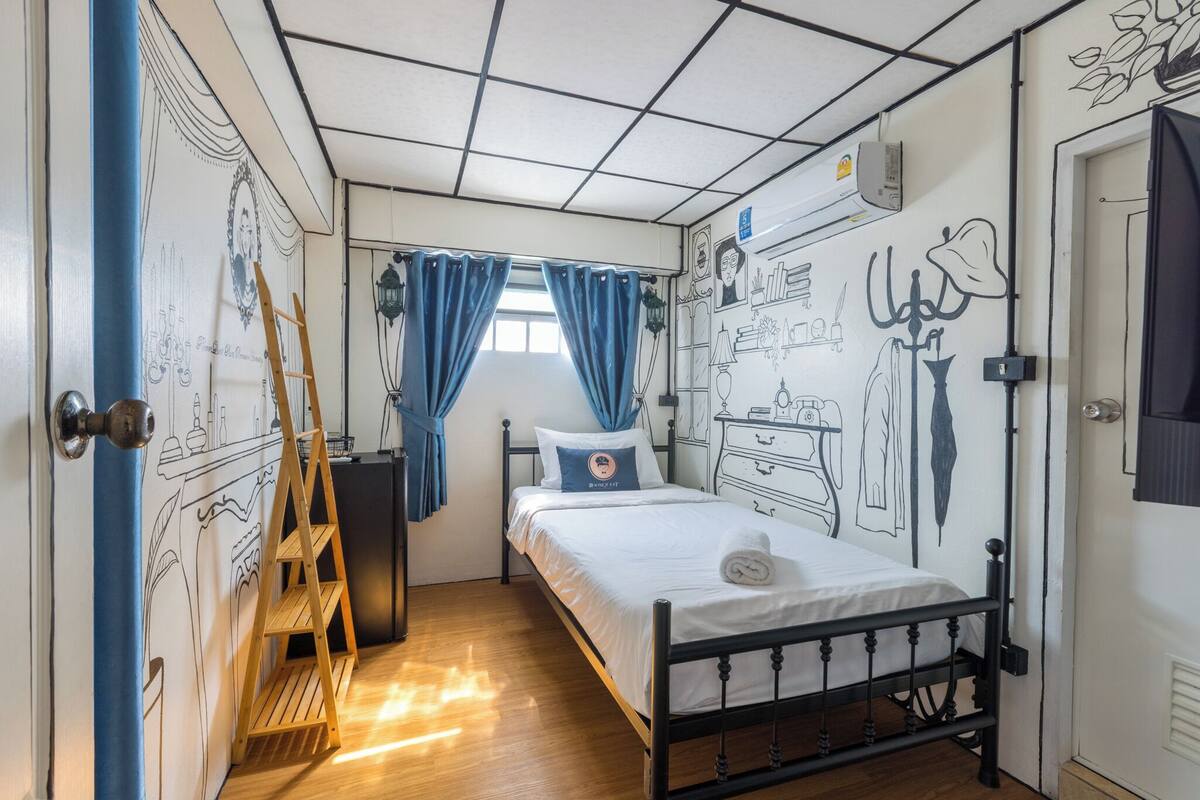Une chambre à coucher avec un lit, une échelle, une fenêtre avec des rideaux et un mur orné de dessins.