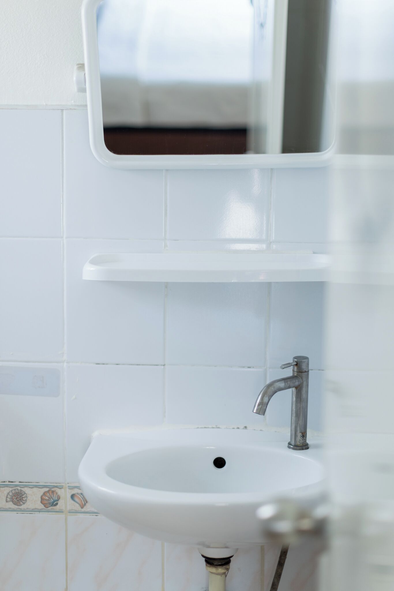 Ein Badezimmer mit einem weißen Waschbecken, einem Spiegel und einer gefliesten Wand.