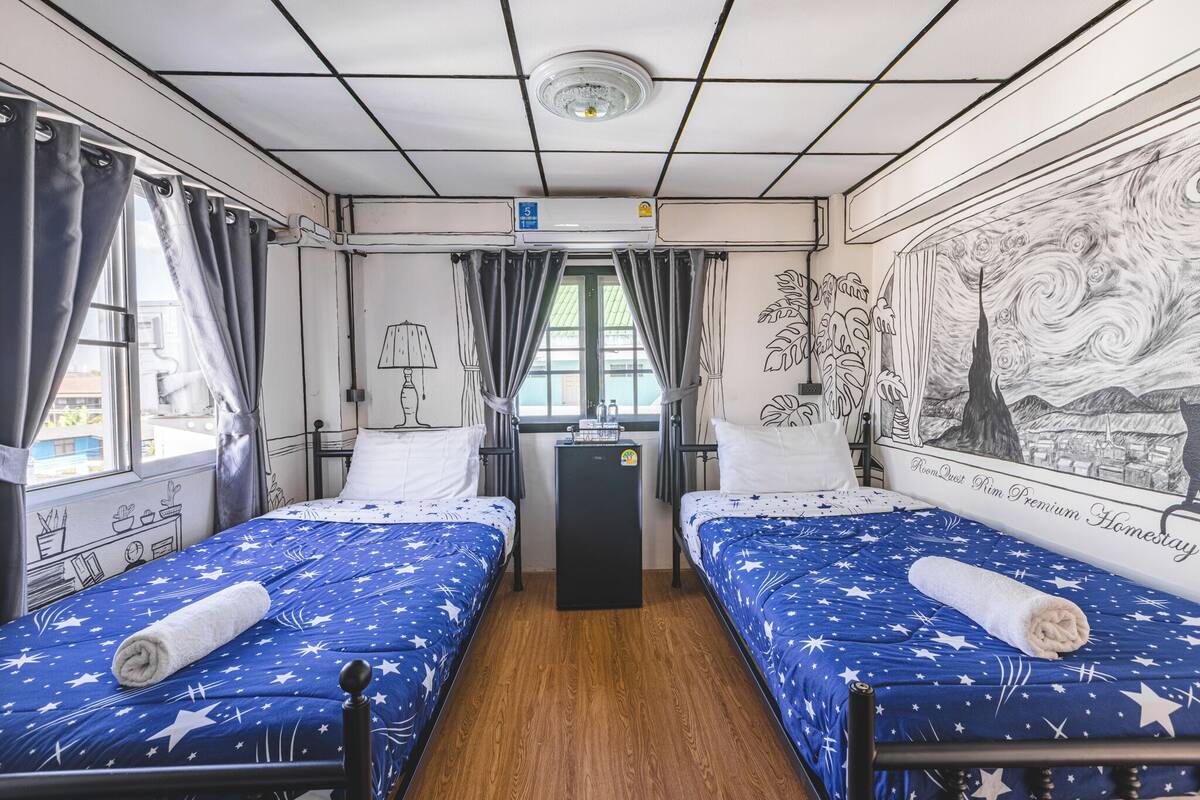 Une chambre avec deux lits, une petite table, une horloge murale et une fenêtre avec des rideaux.
