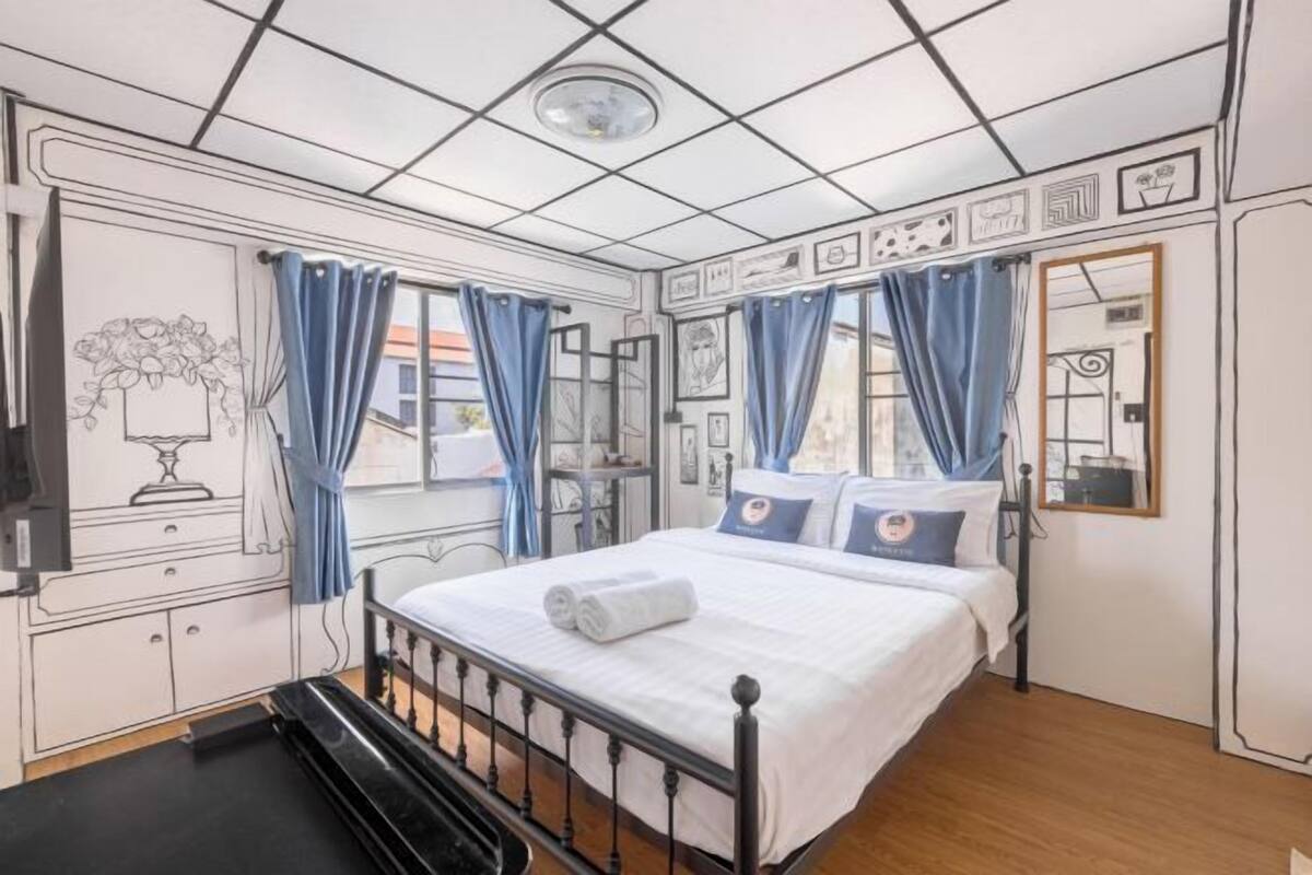 Une chambre à coucher avec un lit, des rideaux, une commode, un miroir et des œuvres d’art murales.
