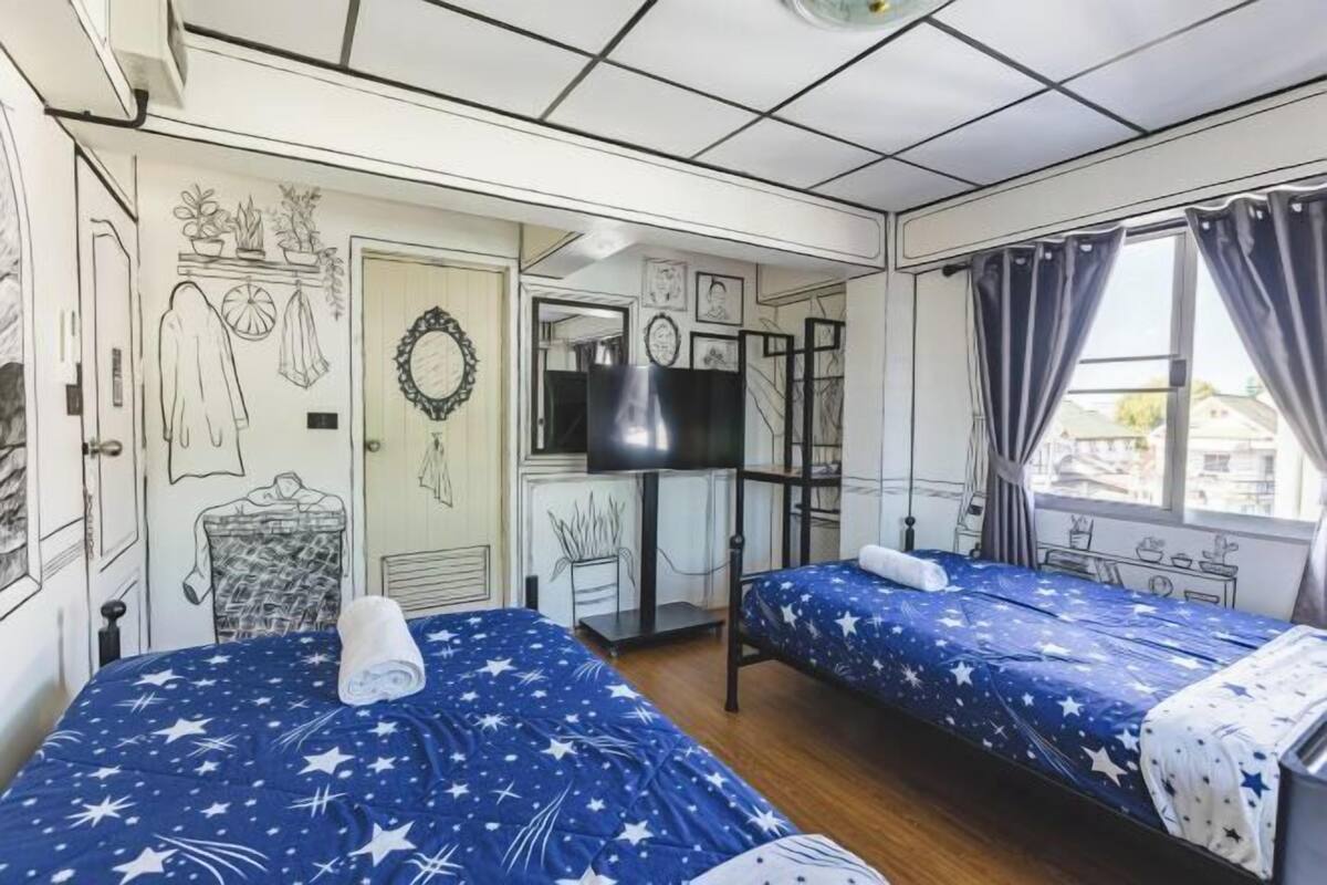 Une chambre avec deux lits, une télévision, une armoire et une fenêtre avec des rideaux.