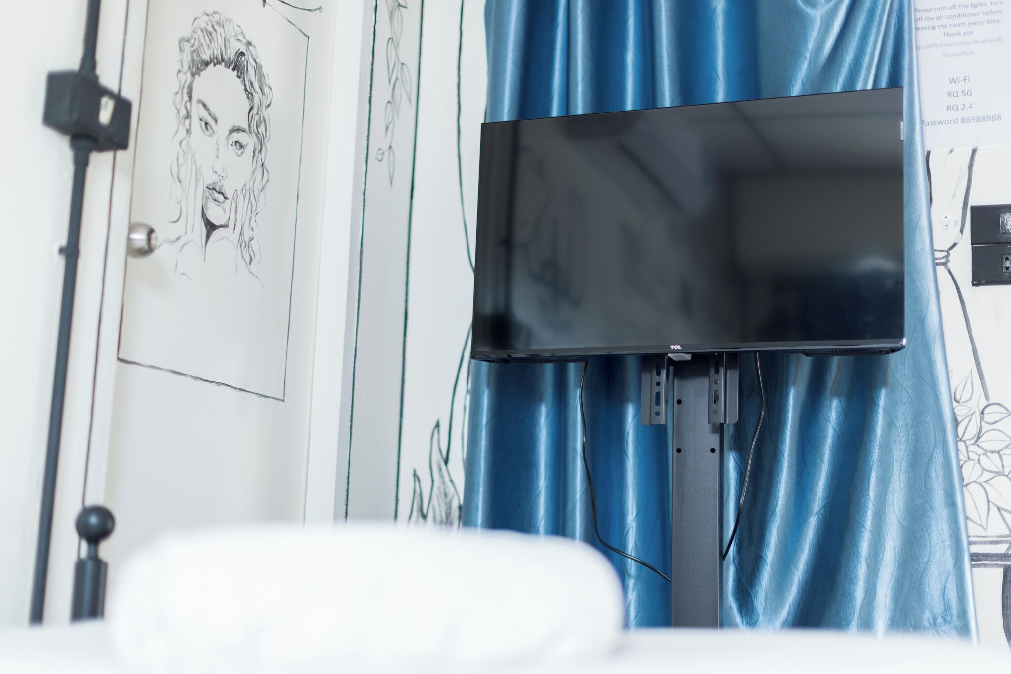 Una habitación con televisor de pantalla plana en la pared, una puerta decorada con un boceto y una cortina azul.