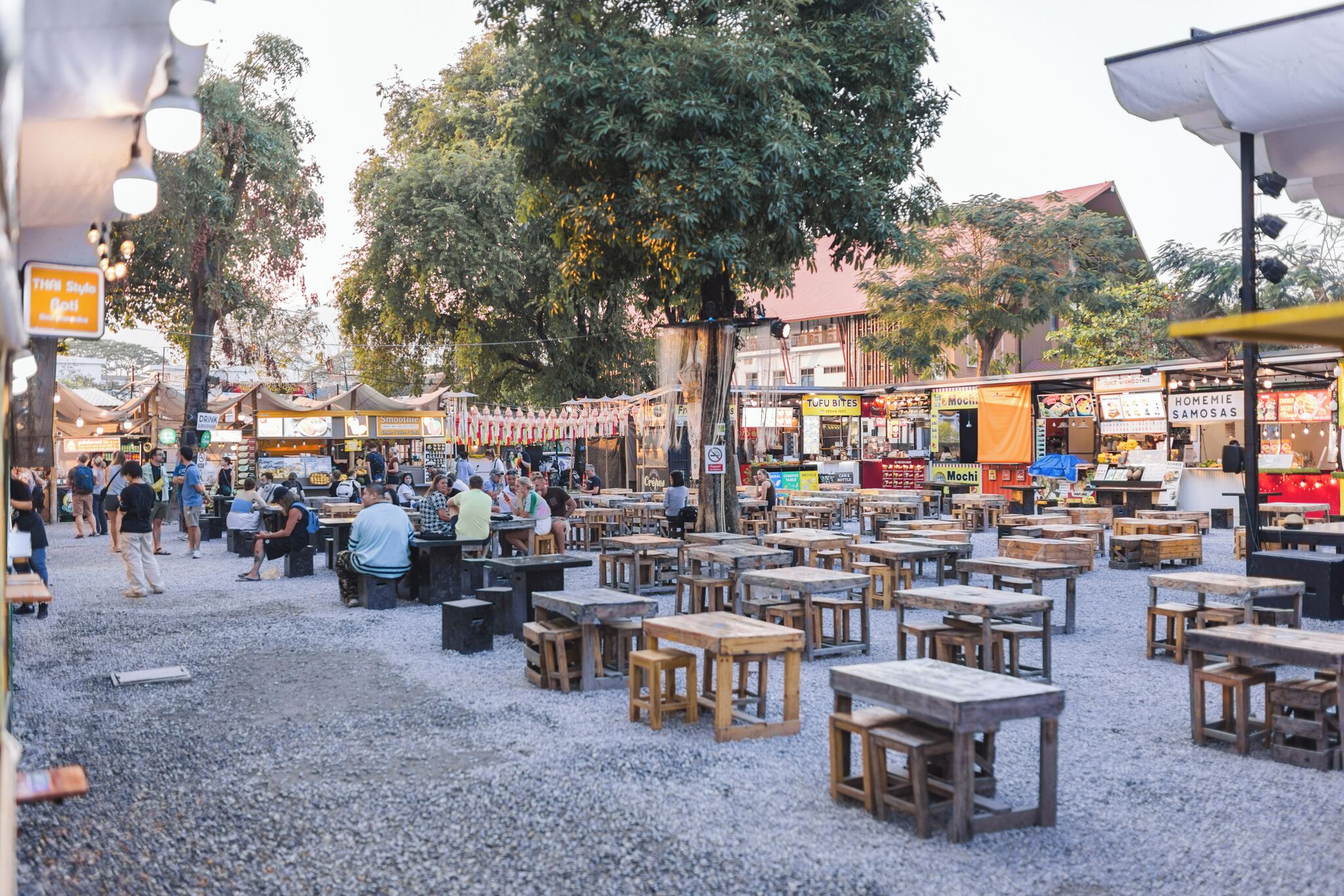 Un marché en plein air avec des tables et des chaises en bois, entouré de différents stands de nourriture.