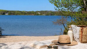 A lakeside view with a picnic setup including a straw hat, sunglasses, a water bottle, and a book on a blanket. - Charlevoix Lakefront Cottage (Charlevoix)